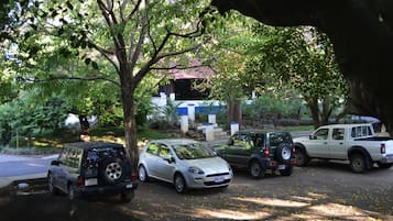 A parking area with several vehicles, including a white compact car and a green SUV, parked under trees.
