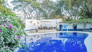 A swimming pool with a patio area, surrounded by lush greenery and a white wall with butterfly decorations. - Hotel Aeropuerto (San Antonio)