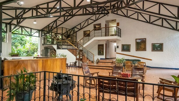 A spacious lobby with a high ceiling, wooden staircase, and multiple seating areas. - Hotel Aeropuerto (San Antonio)