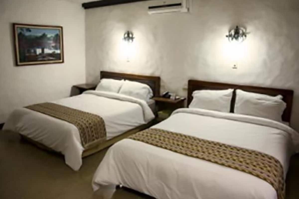 A hotel room with two beds, a painting on the wall, and two wall-mounted lights.