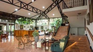 Un vestíbulo amplio con techo alto, mobiliario de madera, un sofá verde y una escalera.