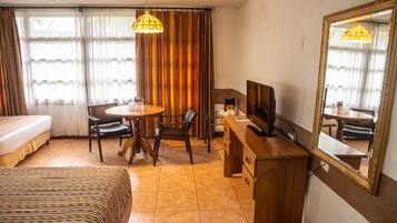 Una habitación de hotel con cama, escritorio con computadora, silla, mesa y un espejo grande.
