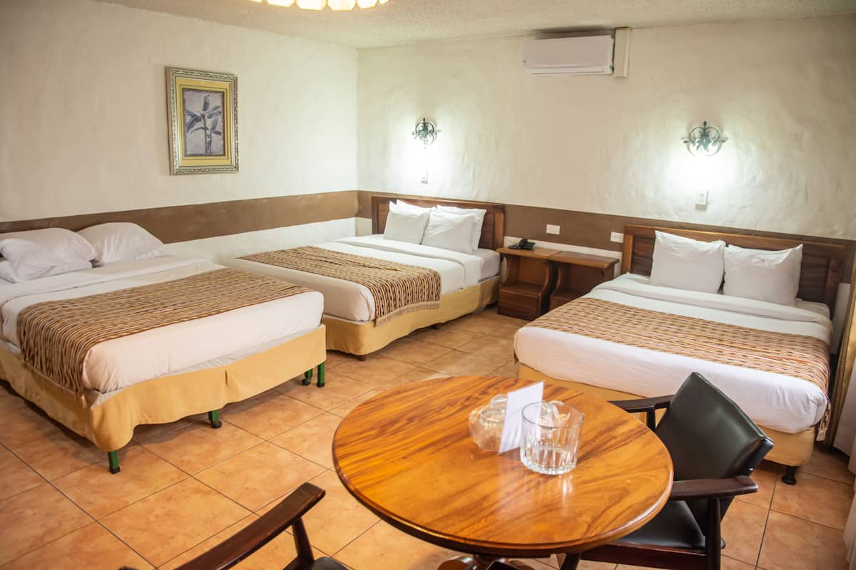 A hotel room with three beds, a round wooden table, and a small side table.