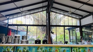 A restaurant with a bar area, large windows, and a view of greenery outside. - Hotel Aeropuerto (San Antonio)
