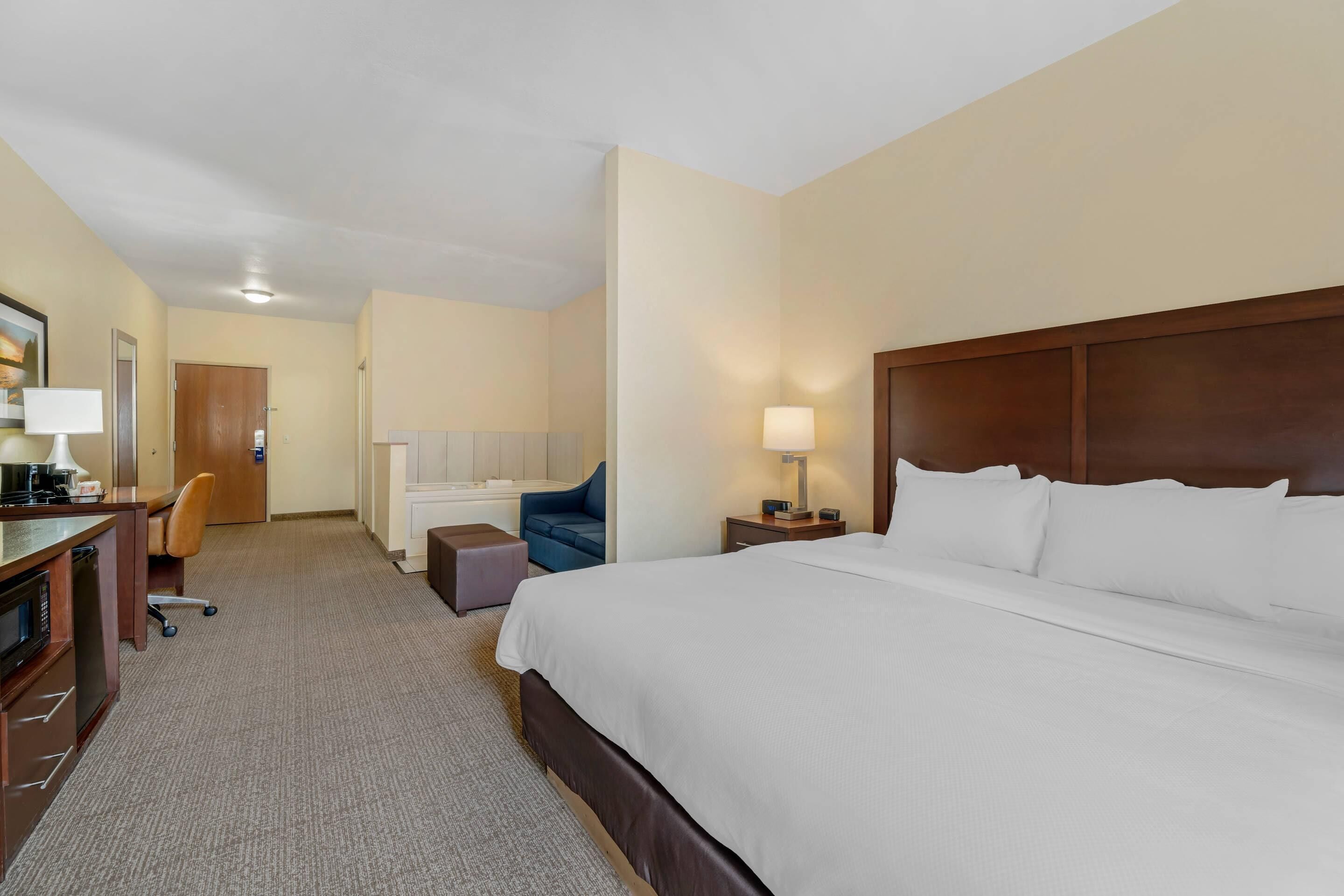Une chambre d’hôtel avec un grand lit, un bureau avec une lampe, une chaise, une petite table et un canapé.