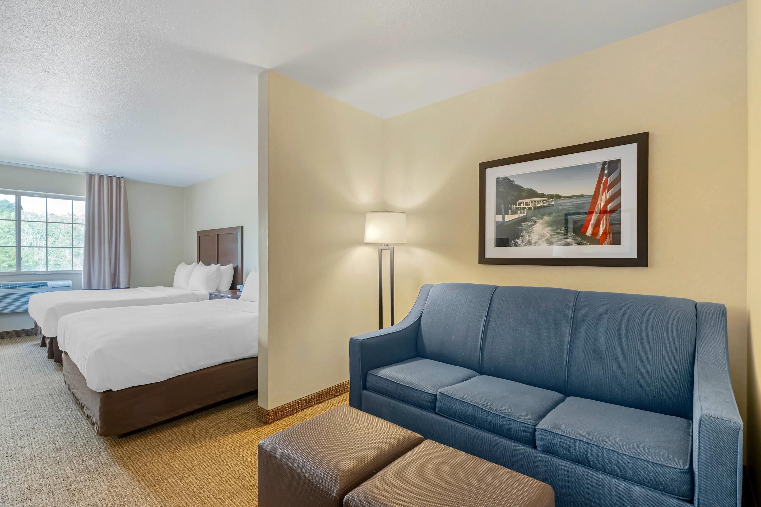 A hotel room with a large bed, two smaller beds, a blue sofa, a lamp, and a framed picture on the wall.