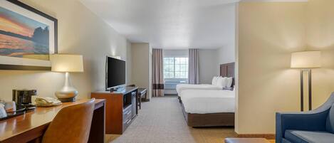 A hotel room with a desk, chair, television, two beds, a sofa, and a window with curtains.