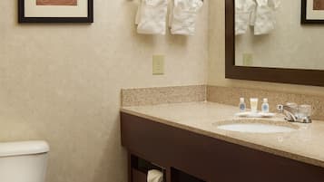 A bathroom with a toilet, sink, mirror, towel rack, and framed artwork on the wall.