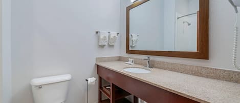Un baño con inodoro blanco, lavamanos con espejo y secador de pelo en la pared.