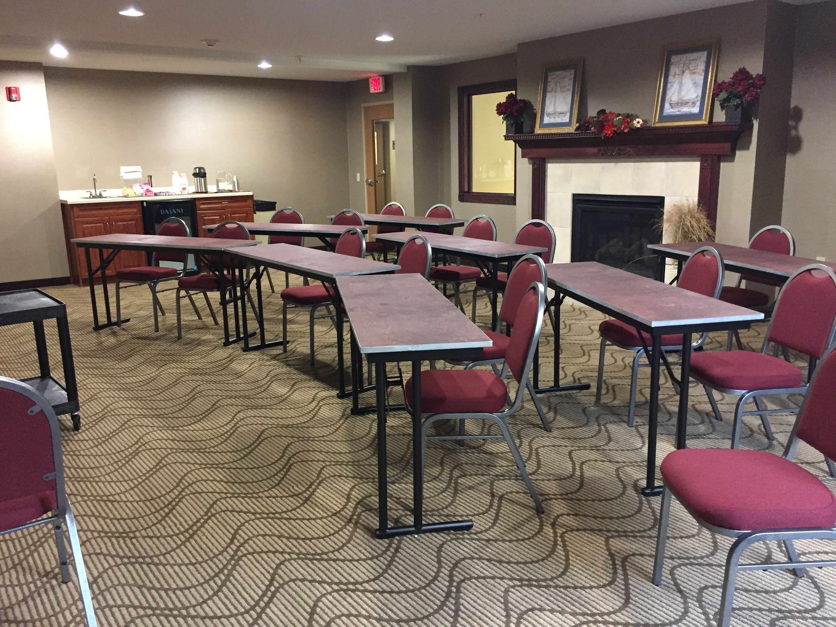 A conference room with tables and chairs, a fireplace, and a kitchen area.