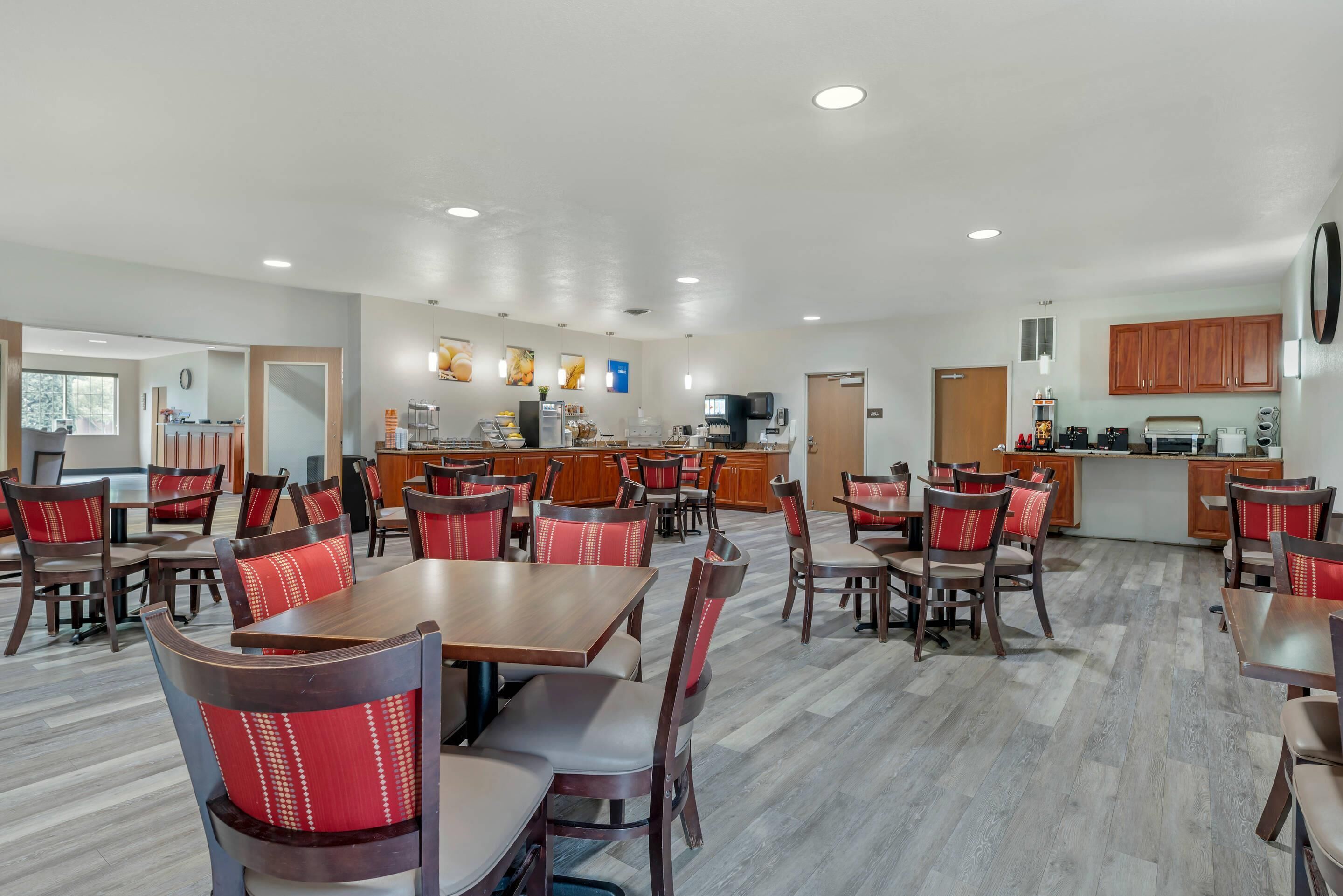 Un comedor amplio con mesas y sillas de madera, una cocina al fondo, y un diseño moderno y limpio.
