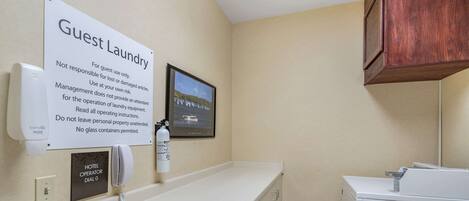 Un espace buanderie à la disposition des clients, avec un panneau indicateur, un téléphone et un tableau accroché au mur.