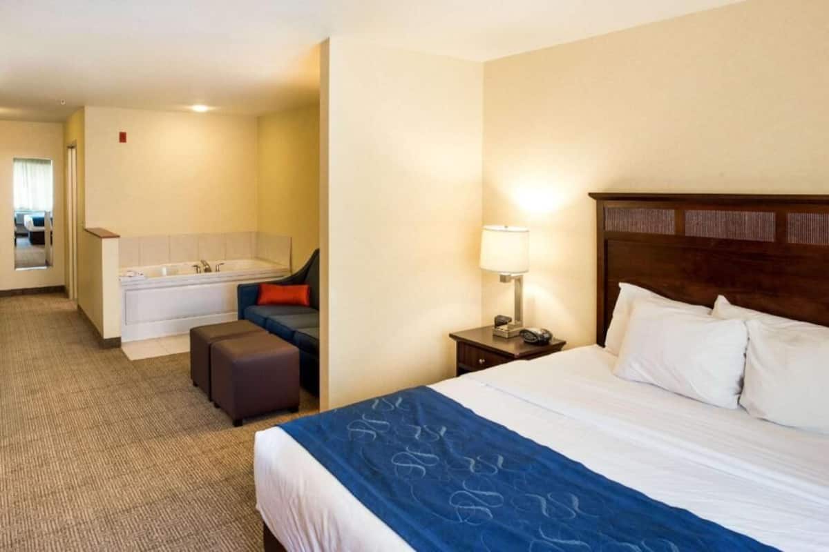 A hotel room with a bed, a desk, a lamp, a chair, and a small table.