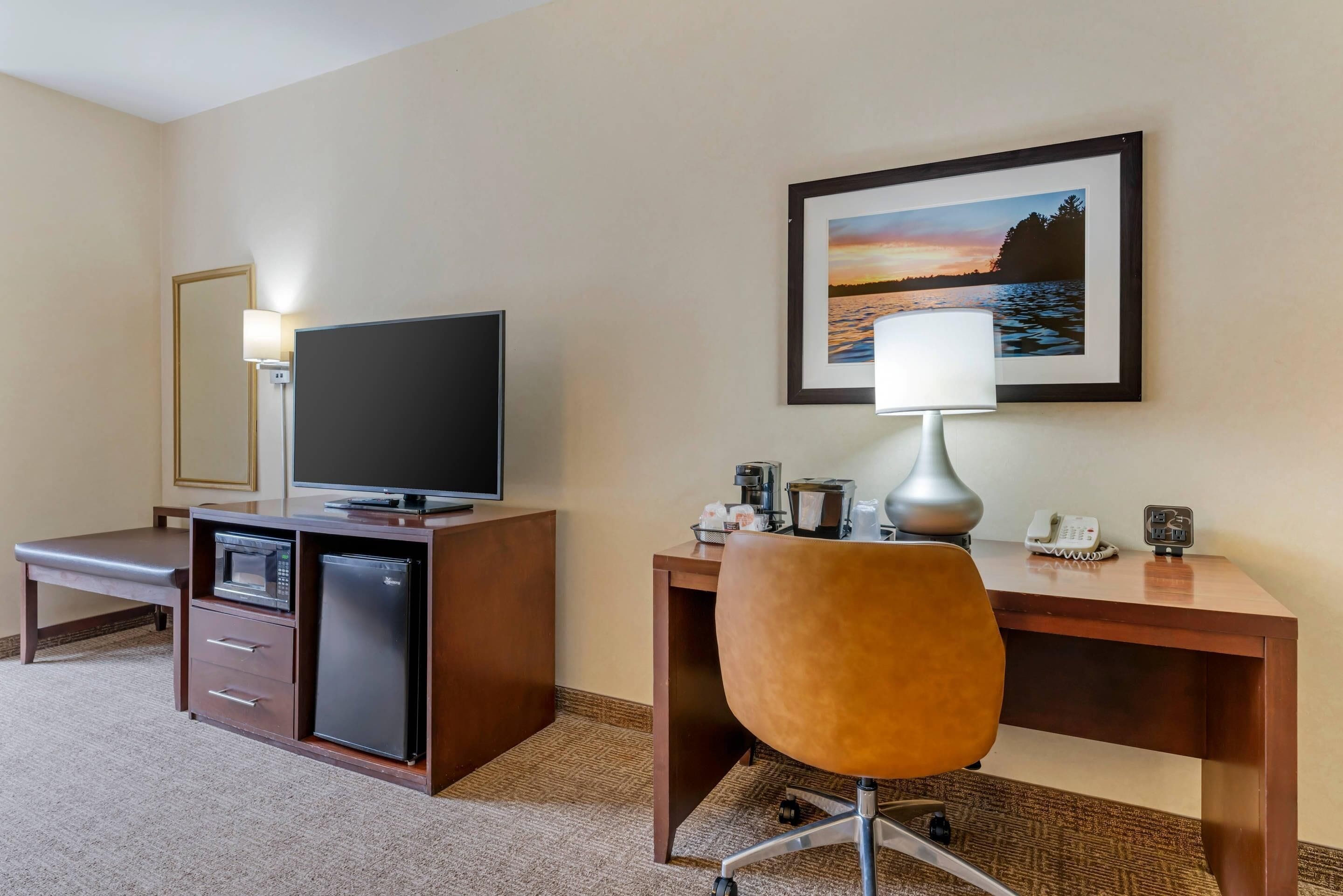 Une chambre d’hôtel équipée d’un bureau, d’une télévision, d’un four à micro-ondes, d’un réfrigérateur, d’une chaise, d’une lampe et d’un tableau encadré au mur.
