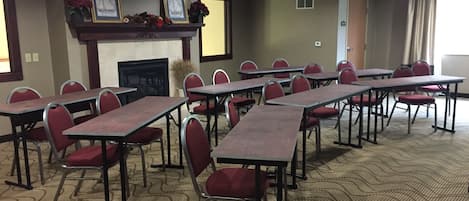 A conference room with long tables and red chairs, a fireplace, and framed artwork on the wall.
