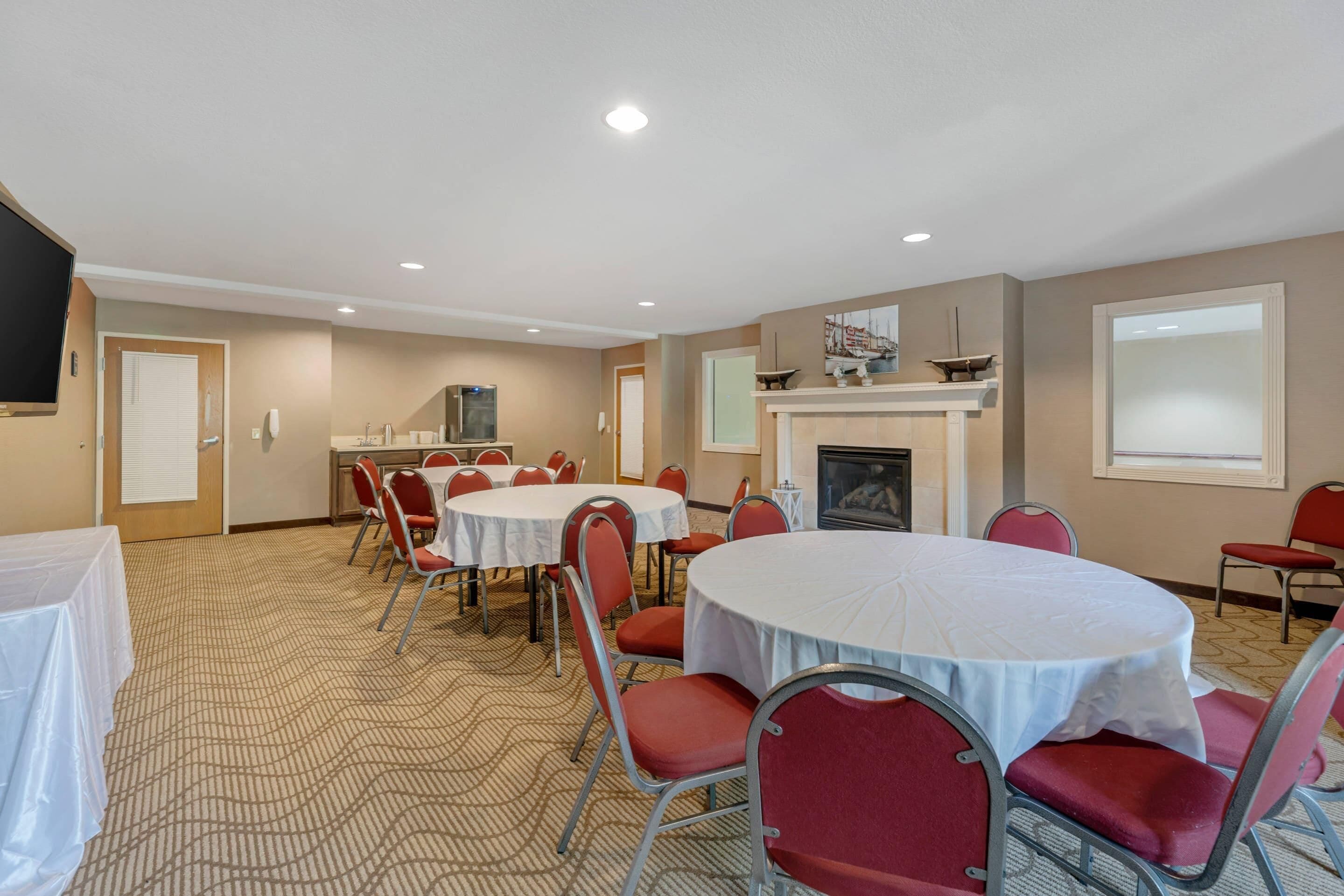A conference room with round tables and red chairs, a fireplace, and a television on the wall.