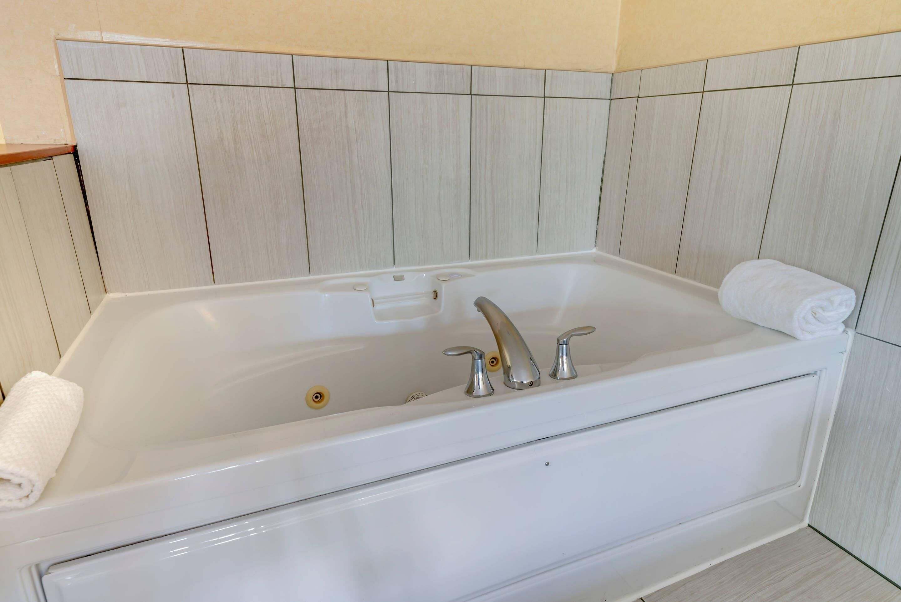 Una bañera blanca con dos llaves y un panel de control, frente a una pared con azulejos.