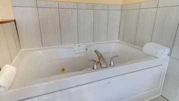 A white bathtub with two faucets and a control panel, set against a tiled wall.