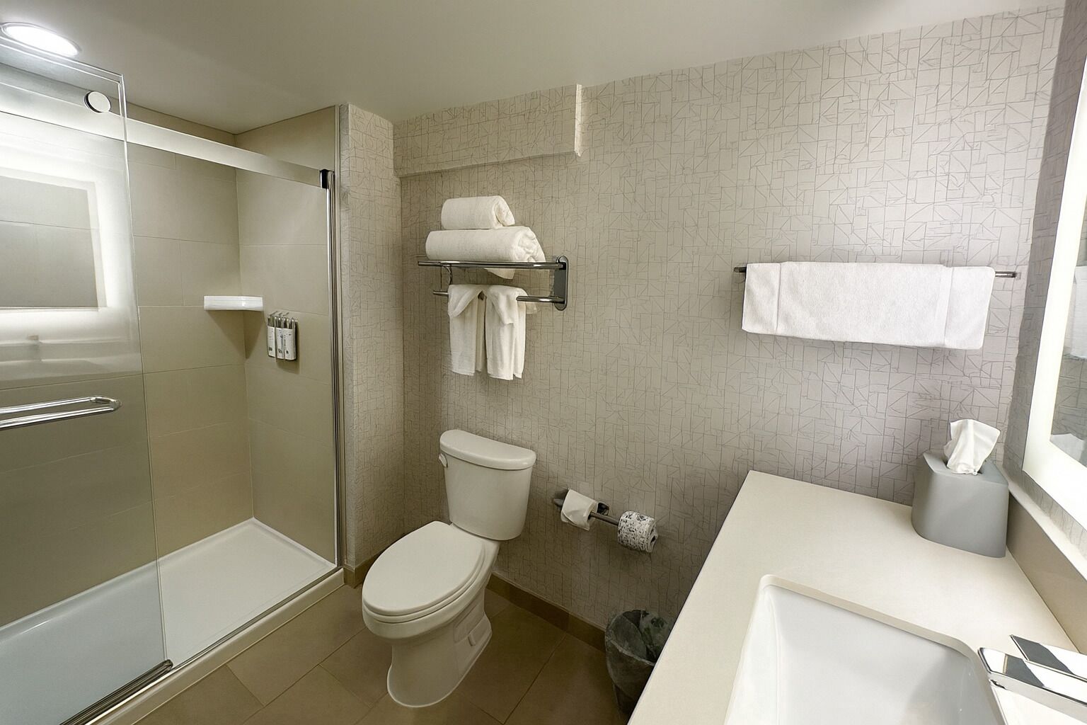 Un baño moderno con cabina de ducha de vidrio, inodoro, lavamanos y toallero.