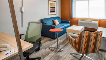 Ein Hotelzimmer mit einem blauen Sofa, einem kleinen Tisch, einem grün gestrickten Stuhl, einem einzigartigen gemusterten Sessel, einer Lampe und einem gerahmten Kunstwerk an der Wand.