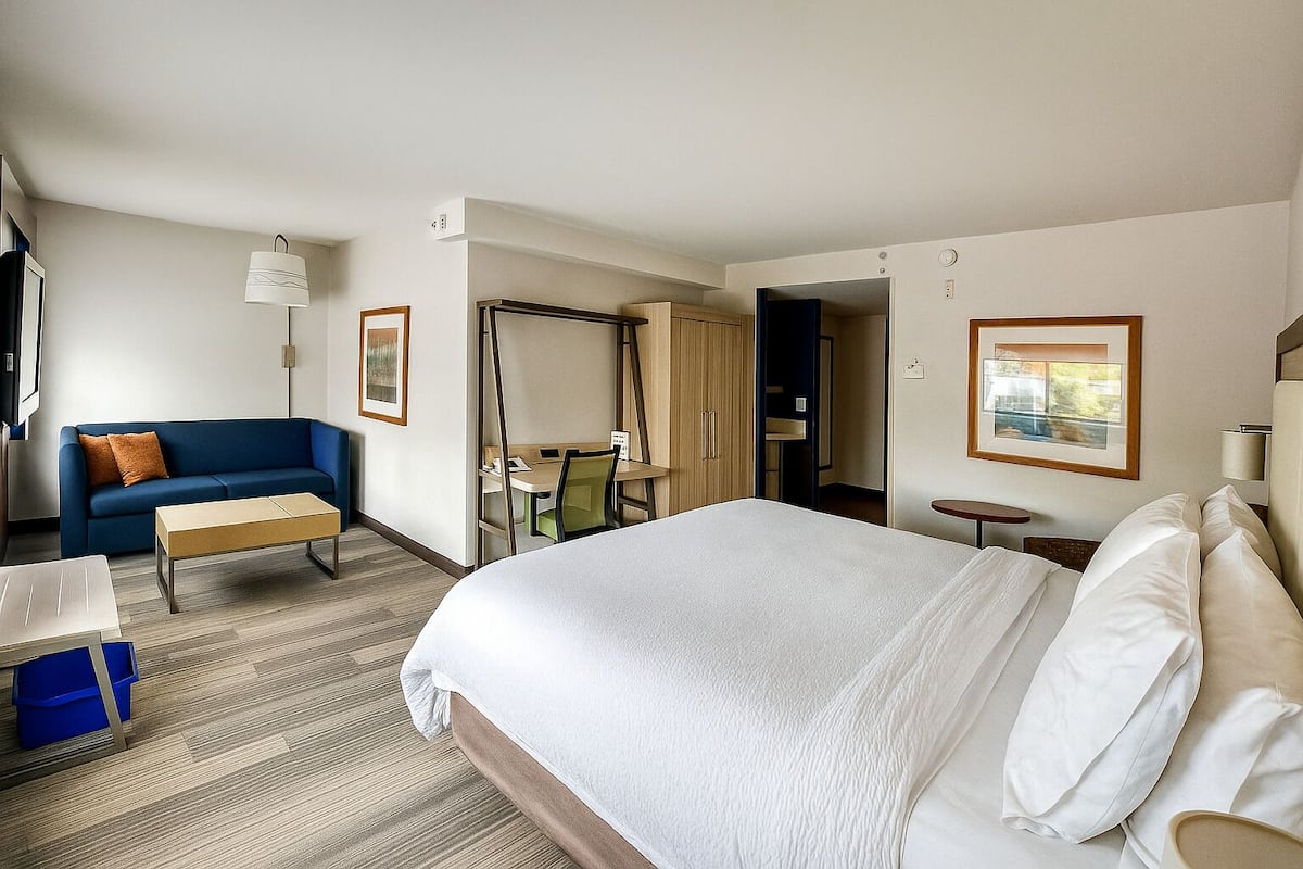 A hotel room with a large bed, a sofa, a desk, and a chair.