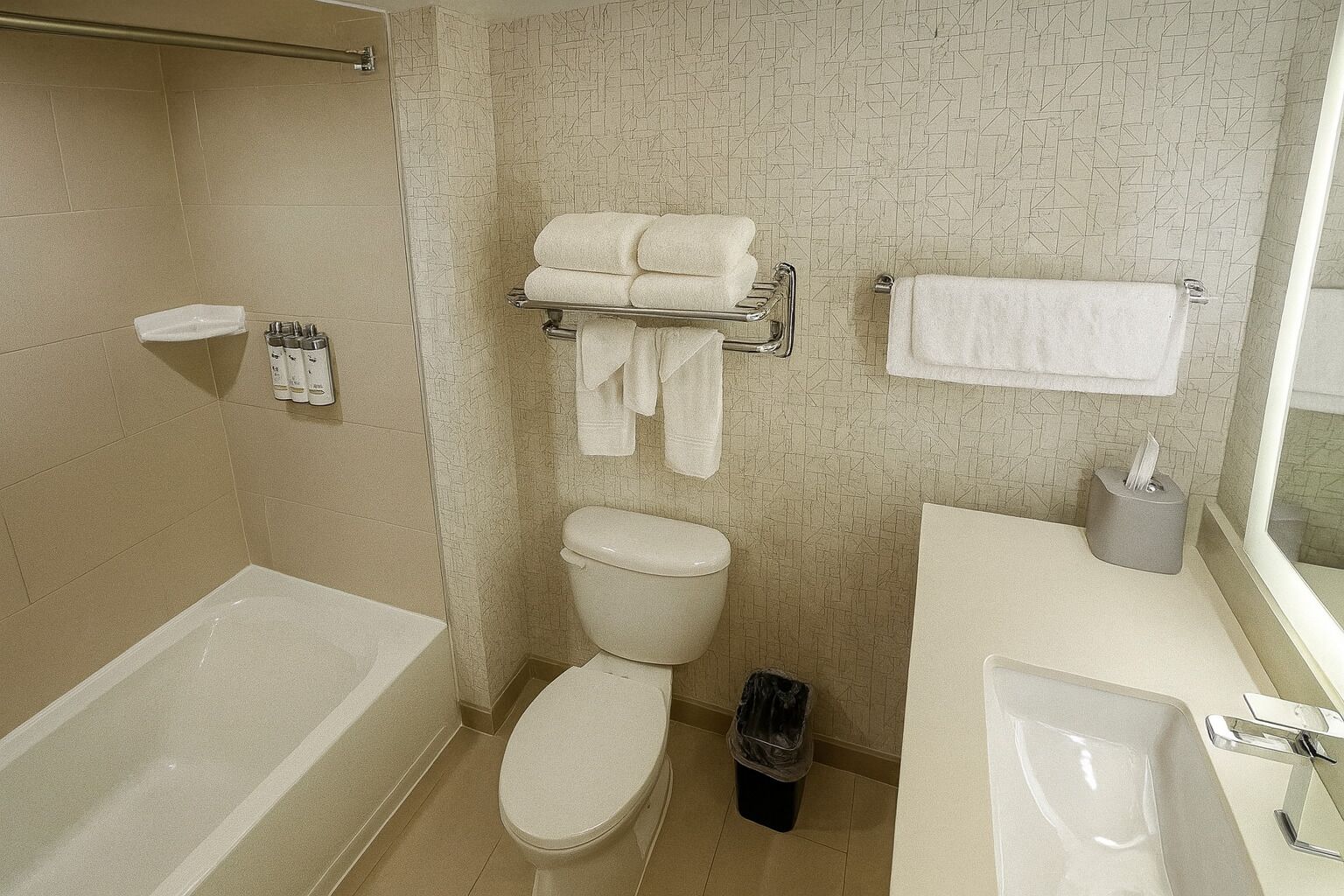 A bathroom with a bathtub, toilet, and sink. There are towels hanging on a rack and a trash bin.