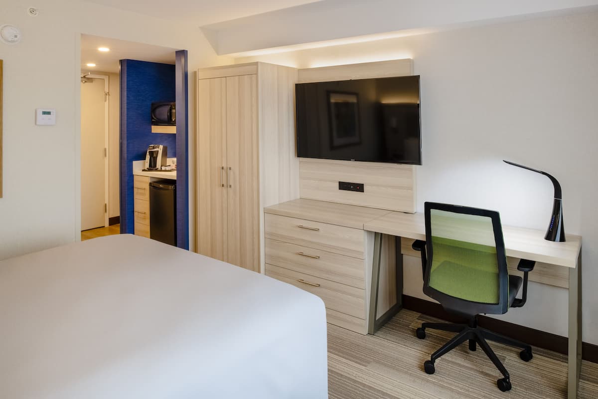 A hotel room with a bed, a desk with a chair, a TV, and a wardrobe.