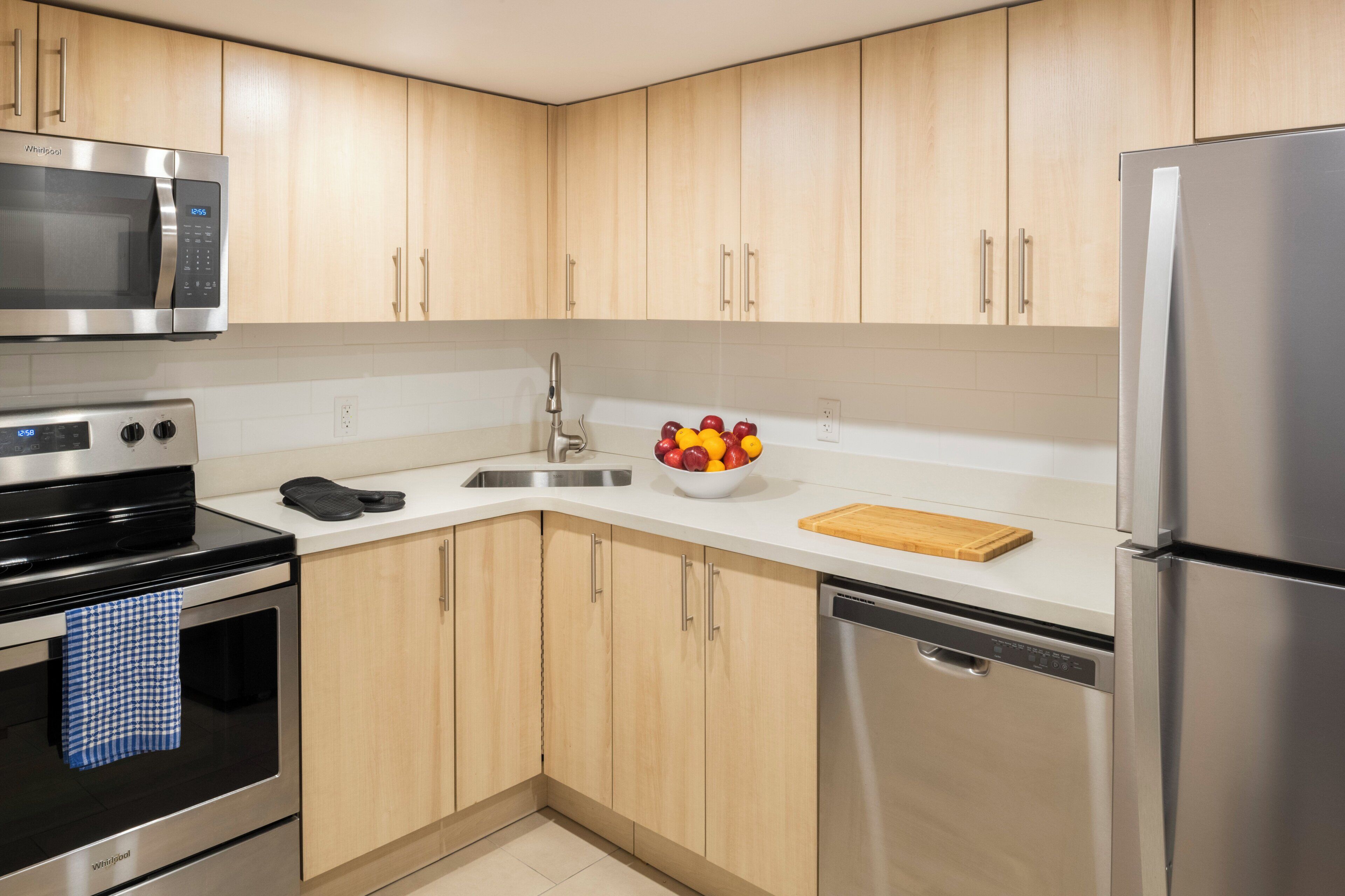 Een moderne keuken met roestvrijstalen apparatuur, houten kastjes en een schaal fruit op het aanrecht.