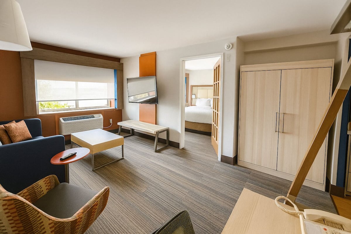 A hotel room with a sofa, a small table, a TV, a bed, a wardrobe, and a staircase.