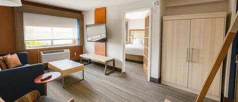 Habitación de hotel con sofá, una mesita, televisión, cama, armario y una escalera.