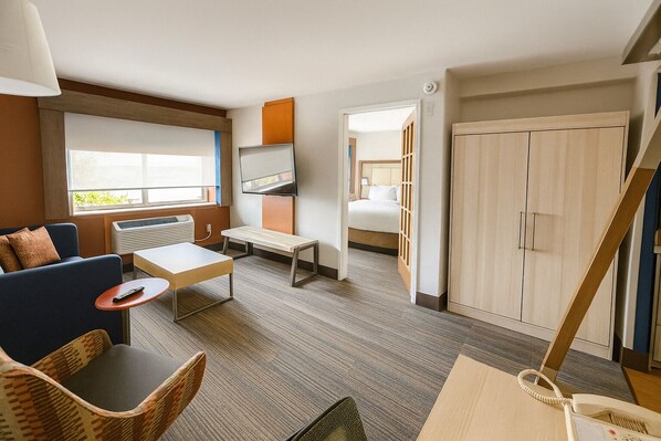 A hotel room with a sofa, a small table, a TV, a bed, a wardrobe, and a staircase.