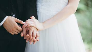 Un gros plan d’un couple se tenant la main, l’homme portant un costume noir et la femme une robe blanche.
