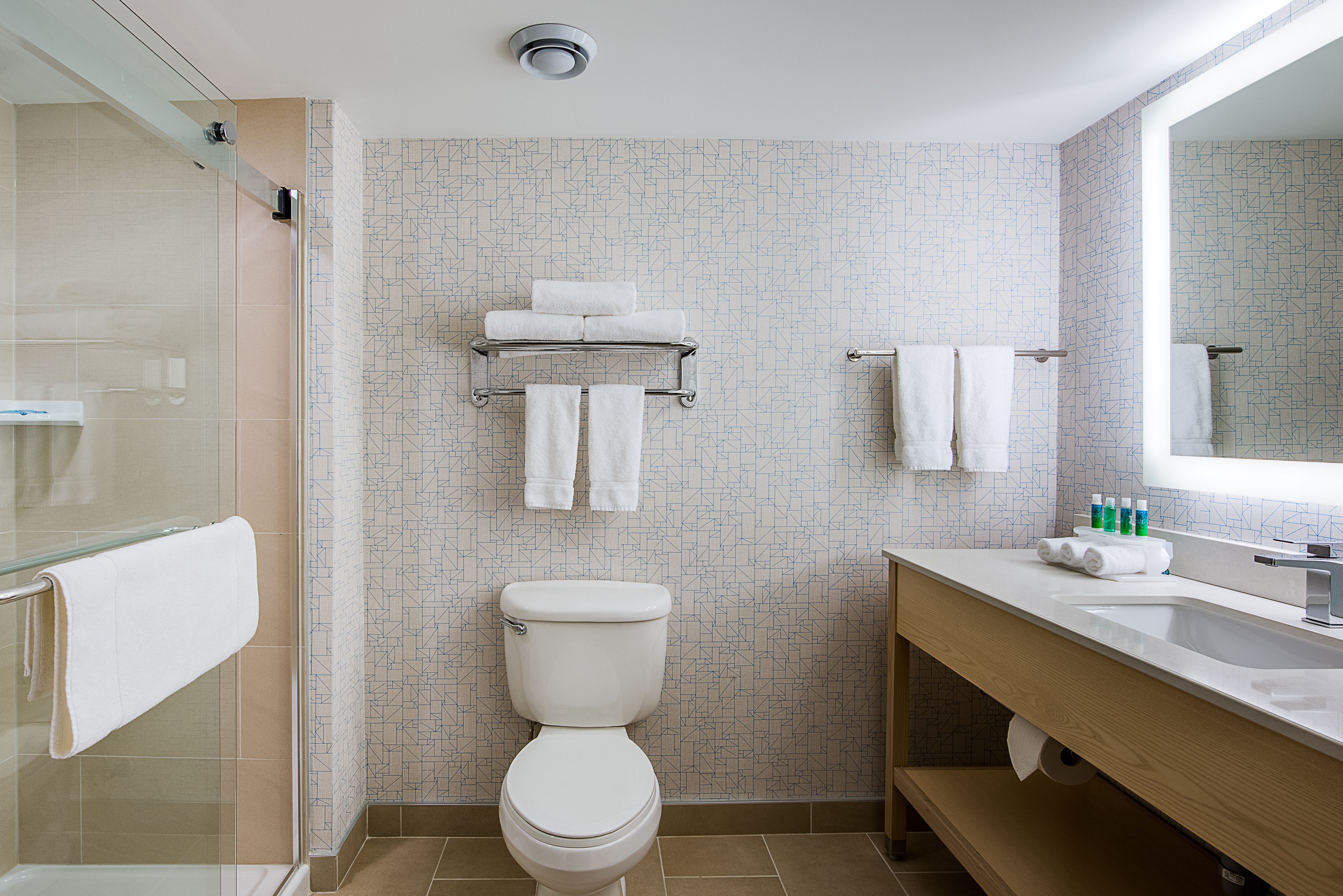 A modern bathroom with a glass shower enclosure, a toilet, a sink with a mirror, and a towel rack with multiple towels.