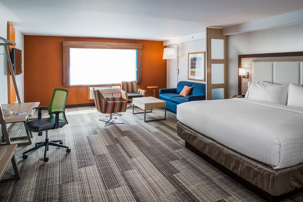 A hotel room with a large bed, a desk with a chair, a sofa, and a small table.
