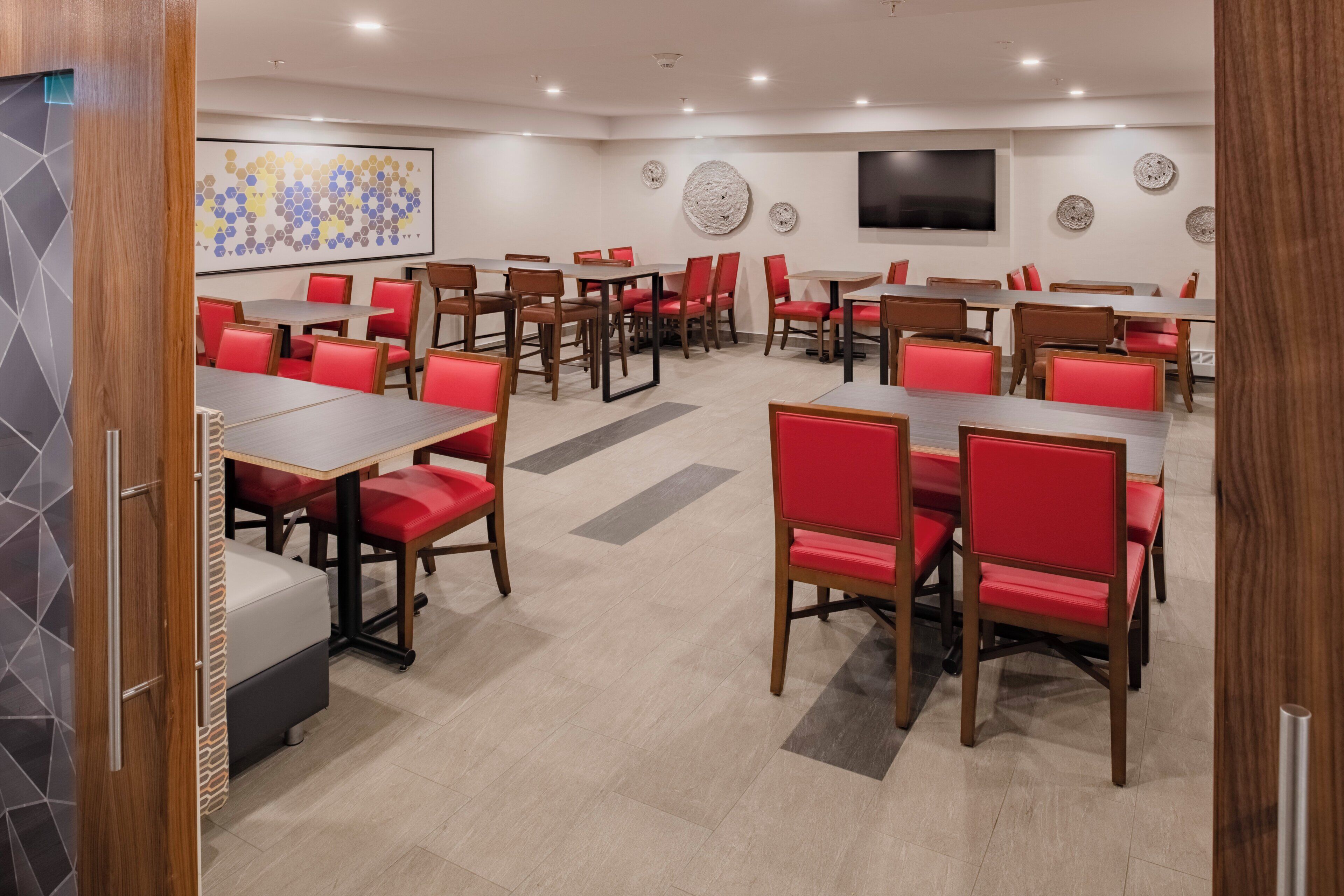 A conference room with multiple tables and chairs, a flat-screen TV mounted on the wall, and decorative wall art.