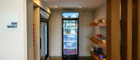 A mini market area with a refrigerated display and shelves stocked with snacks and beverages.