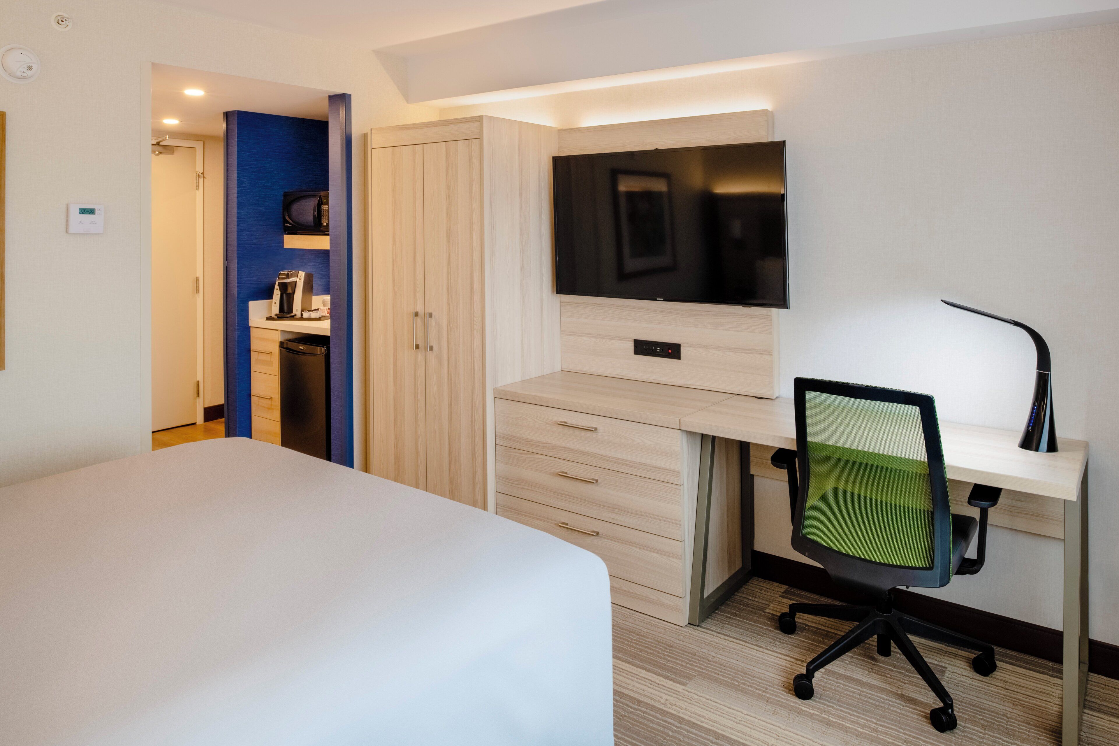 A hotel room with a bed, a desk with a chair, a TV, and a wardrobe.