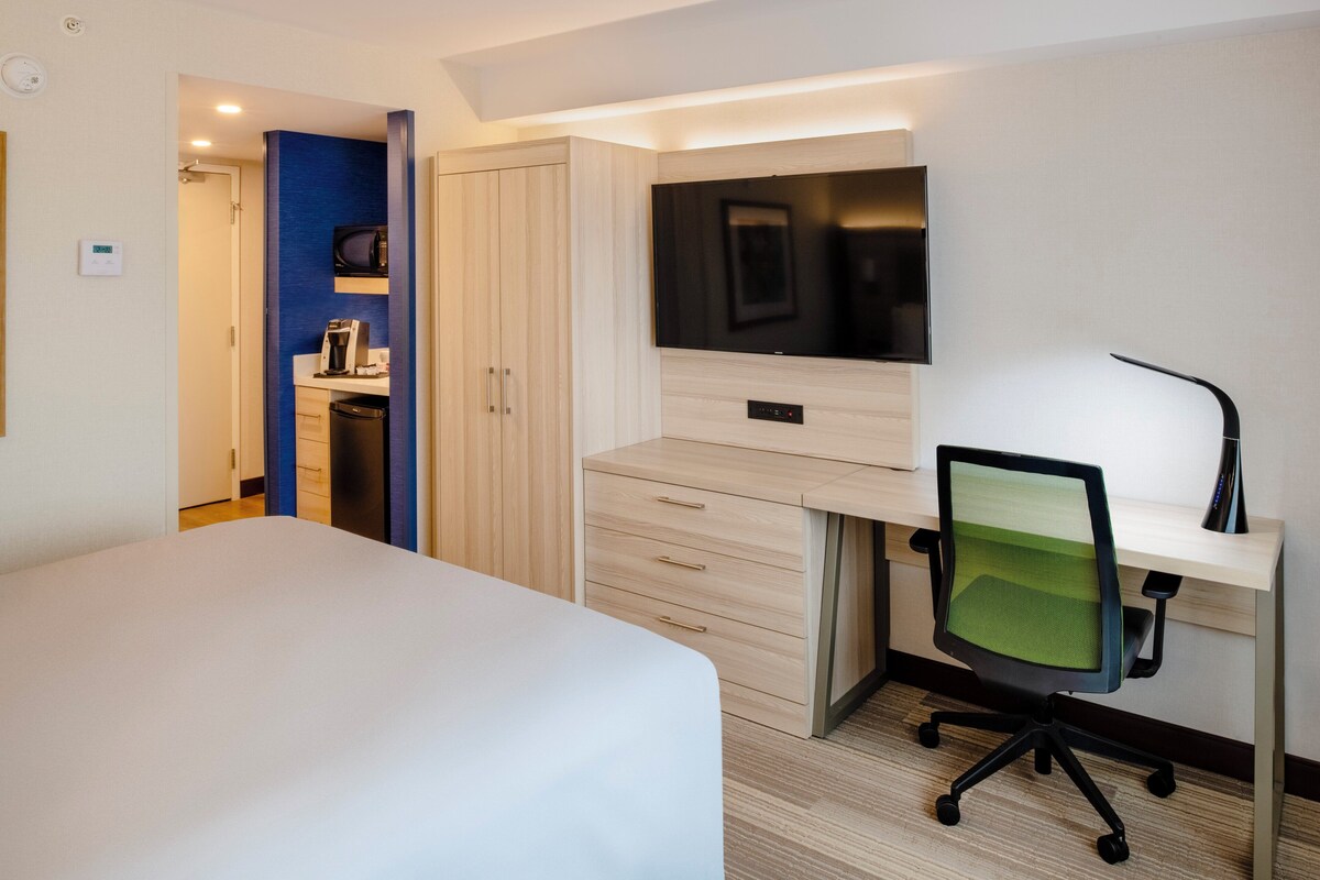A hotel room with a bed, a desk with a chair, a TV, and a wardrobe.