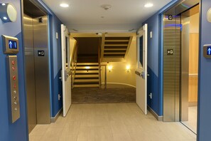 A hotel elevator with a control panel, a sign indicating the direction to the stairs, and a carpeted floor.