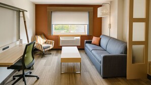 A compact living space with a wooden desk, a cushioned chair, a sofa, and a standing lamp. - Holiday Inn Express & Suites Halifax - Bedford by IHG (Halifax)