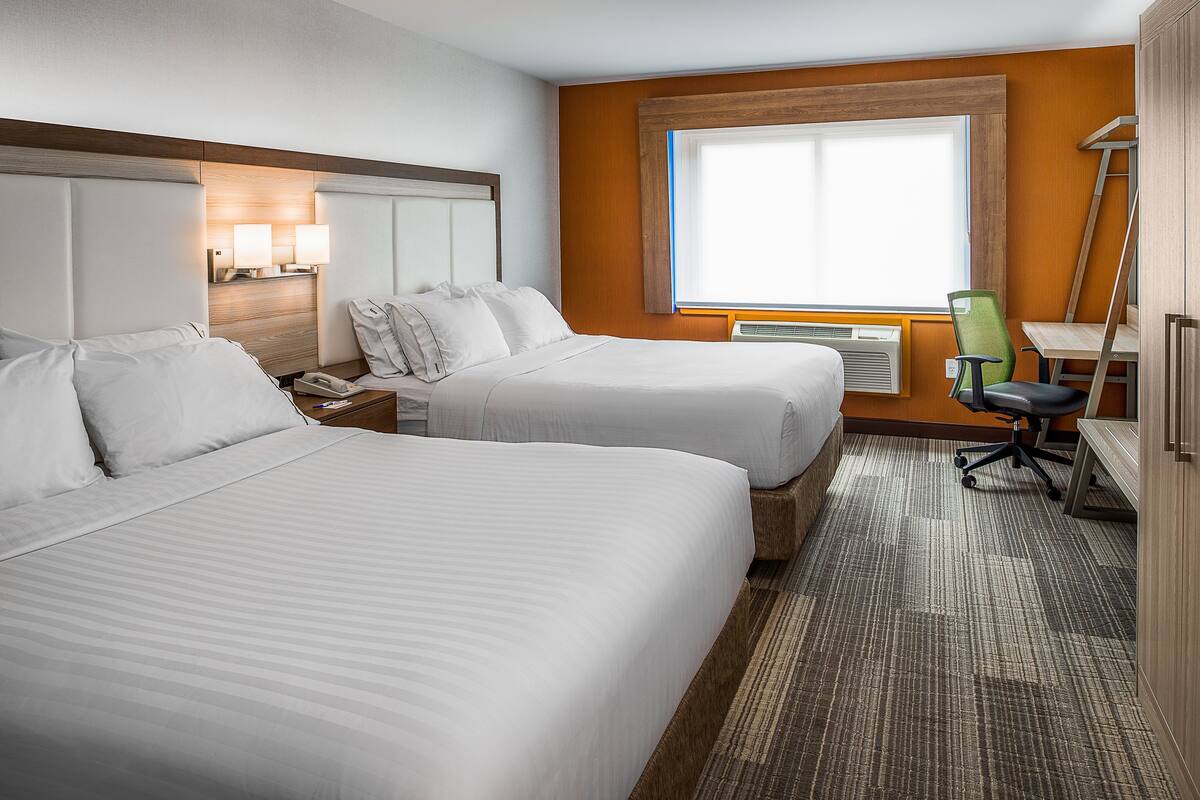 A hotel room with two beds, a desk, a chair, a lamp, and a window.