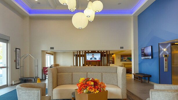 A hotel lobby with a sofa, chairs, a flower arrangement, a television, and an elevator.