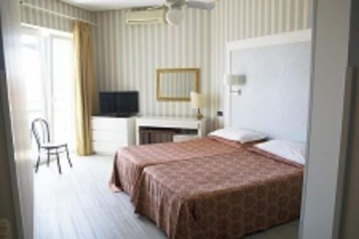 Een hotelkamer met twee bedden, een bureau met televisie, een stoel en een raam met gordijnen.