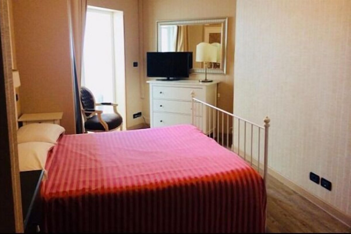 Una habitación de hotel con cama, una silla, cómoda, televisor y espejo.