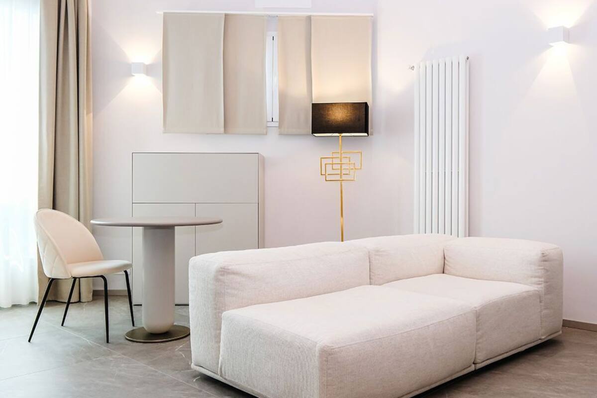 Een moderne woonkamer met een bank, een ronde tafel en een stoel. Er zijn wandlampen en een vloerlamp.