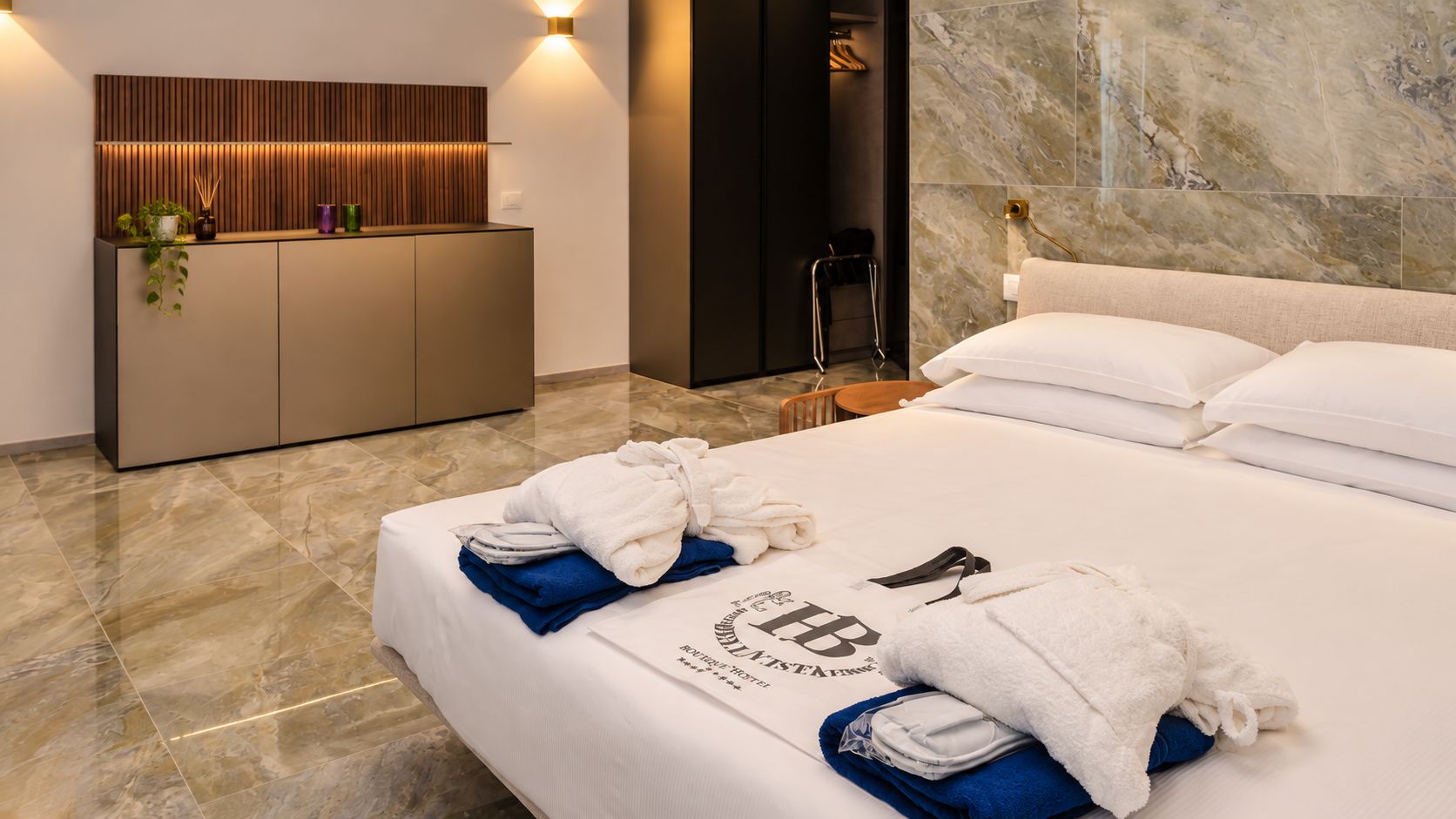 Habitación de hotel con cama, minibar, luz empotrada en la pared y suelo de mármol.