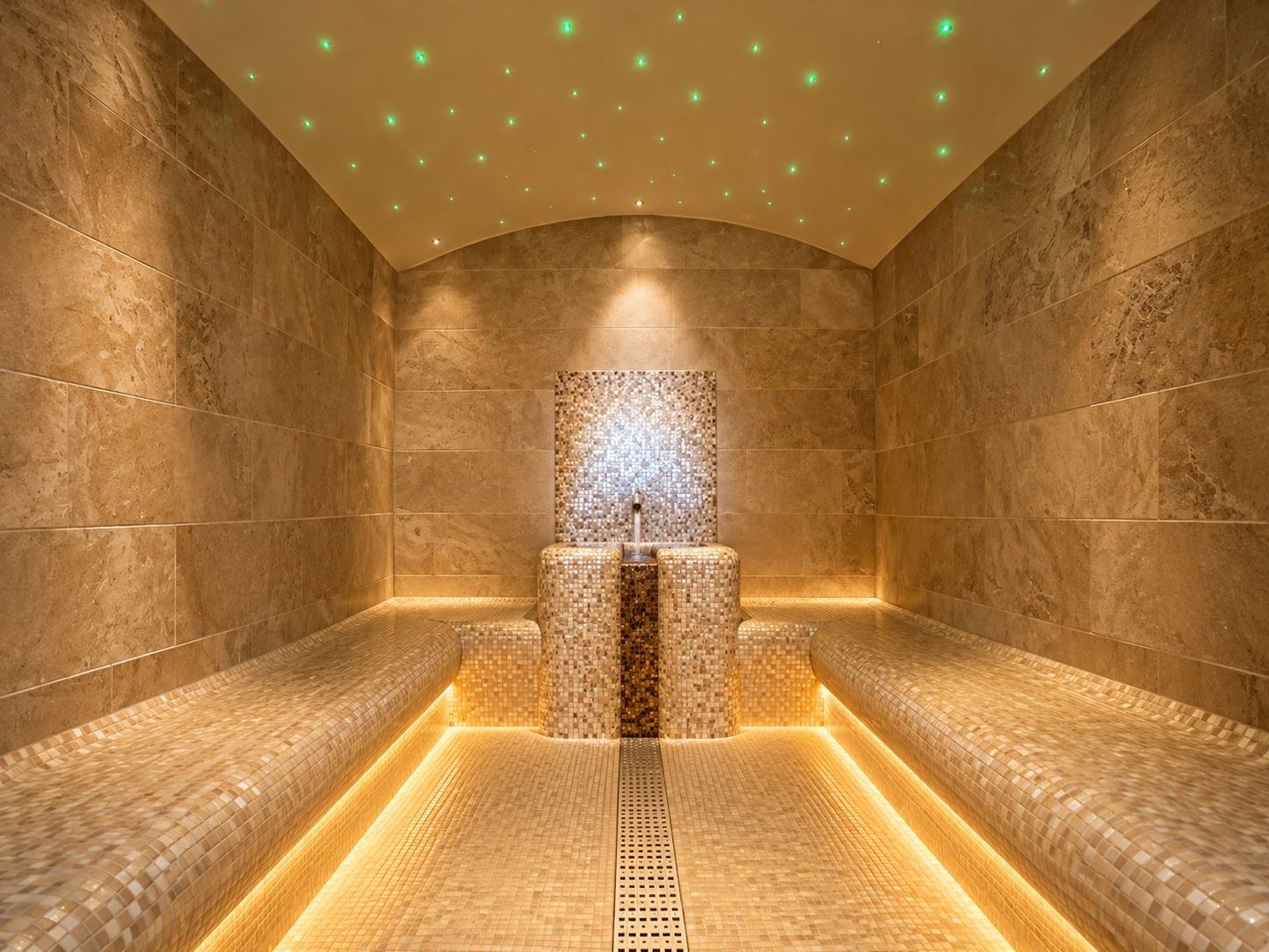 Un cuarto de spa con una fuente central, paredes con azulejos y bancos a los lados.