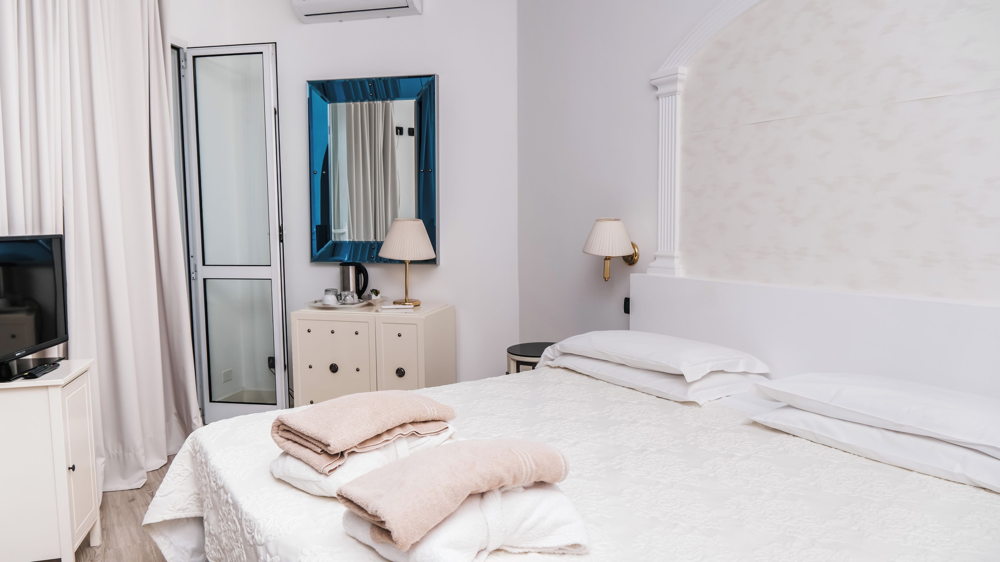 Ein Hotelzimmer mit Bett, Fernseher, Kleiderschrank, Spiegel und Fenster.