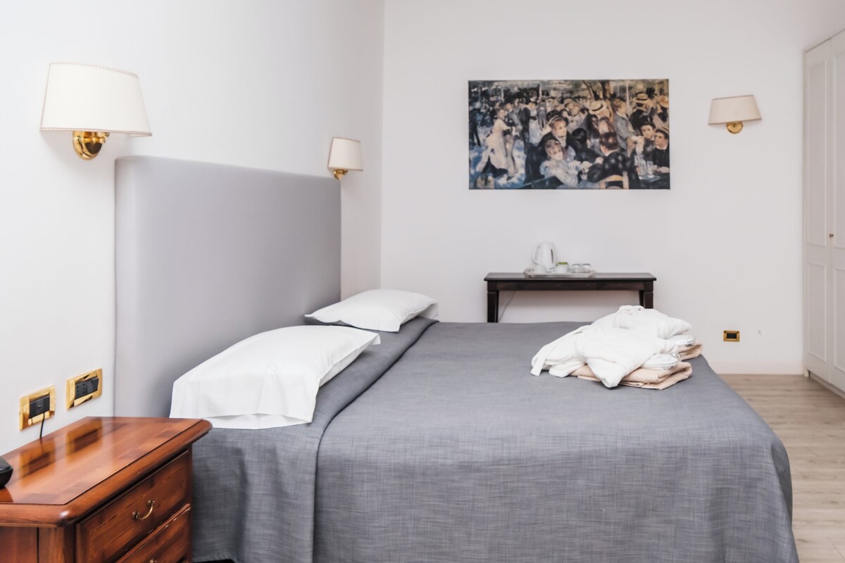Een slaapkamer met een bed, bedlampjes, een nachtkastje, een schilderij en een kledingkast.