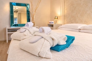 A neatly made bed with folded towels and robes, a bedside table with a lamp, and a mirror reflecting part of the room. - Bellavista Terme Resort & Spa (Montegrotto Terme)